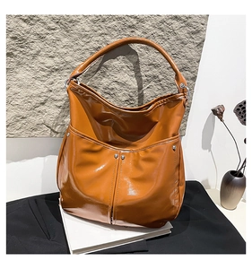 Détail du grand sac cabas marron brillant avec rivets métalliques sur fond de pierre épuré