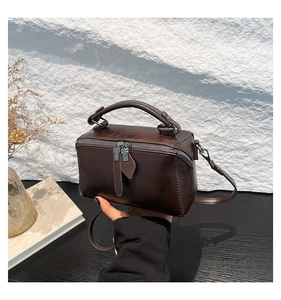 Detailed close-up of dark brown vintage leather square handbag with dual gun-metal zippers