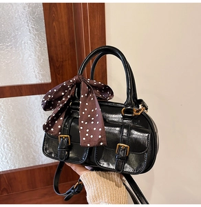 Detail of black glossy PU leather bowling bag with vintage bronze buckles and polka dot scarf