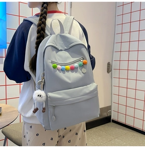 Detail of light gray nylon backpack with colorful pom-poms and white plush toy pendant