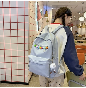 Close-up of light blue backpack with colorful pom-poms and a plush doll pendant detail