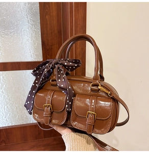 Detail of brown glossy bowling bag featuring front buckle pockets and polka dot scarf