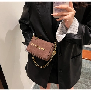 Detail of a brown matte crossbody bag featuring a gold chain and heart metal logo
