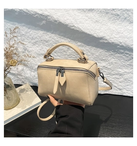 Detail of beige crossbody bag with dual zippers and leather pulls on a wood surface