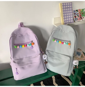Detail of minimalist school backpacks in lavender and pale green with plush ornaments