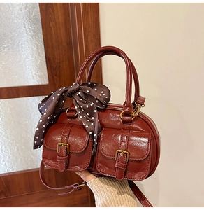Close-up of glossy burgundy Boston bag with front pockets and polka dot scarf
