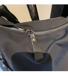 Detail eines glatten Metallreißverschlusses und Lederziehers an einer schwarzen Nylontasche
