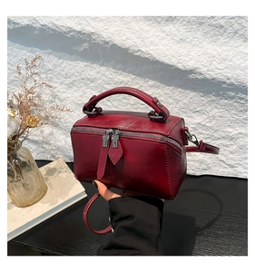 Detailed view of deep red leather cylindrical Boston bag with top handle and strap