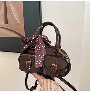 Detail of dark brown glossy bowling bag with gold buckles and polka dot silk scarf