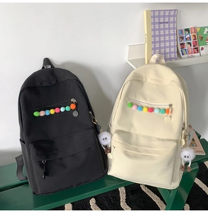 Close-up of black and beige school backpacks with cute plush pendants on a green bench