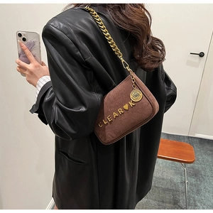 Detail of a brown suede mini bag featuring a gold chain strap and metal logo accent