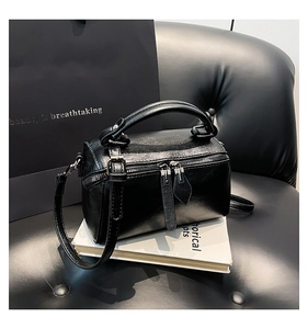 Detail of black polished bucket bag with double zippers and slim handles on a book