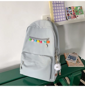 Detail of light blue backpack featuring colorful pom-poms and cute plush charm on a green bench