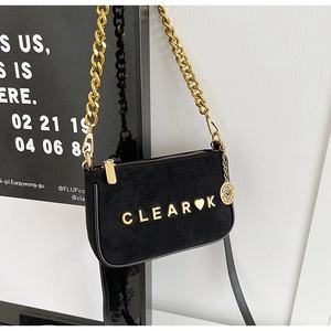 Close-up of black matte suede crossbody bag with gold chain and metal letter plaque