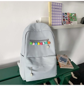 Detail of grey-blue backpack featuring colorful pom-poms on the front zipper pocket