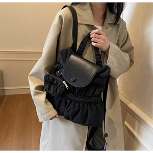 Detail of black pleated nylon backpack featuring a smooth magnetic flap and side pockets