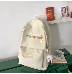 Detail view of off-white canvas backpack with colorful pom-poms and cute plush charm