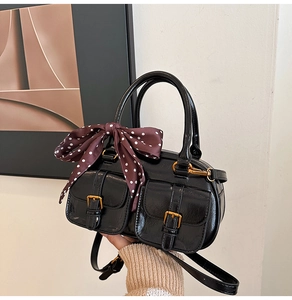 Macro shot of black Boston bag with gold buckle pockets and polka dot silk scarf