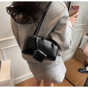 Dettaglio della borsa a spalla nera lucida con mini pochette indossata da una modella