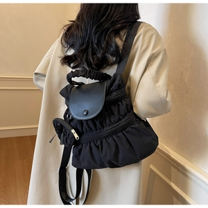 Detail of a black pleated backpack with a matte leather flap and ruffled carry handle