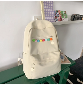 Detail view of beige casual backpack featuring colorful pom-pom zipper pulls on a bench