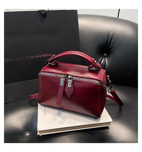 Close-up of glossy red barrel bag with silver zippers and detachable shoulder strap
