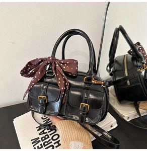 Detail of black glossy handbag with gold buckles, handles and a polka dot silk scarf