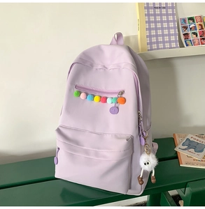 Detail of lavender backpack with colorful pom-pom zipper and white plush monster charm