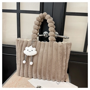 Detail of plush tote bag featuring striped quilting and soft furry ball handles