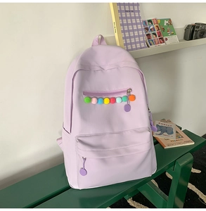 Close-up of light purple canvas backpack featuring colorful pom-poms on the front pocket