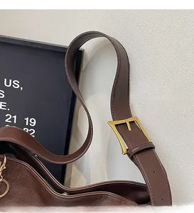 Detail of adjustable long shoulder strap with gold buckle on dark brown leather bag