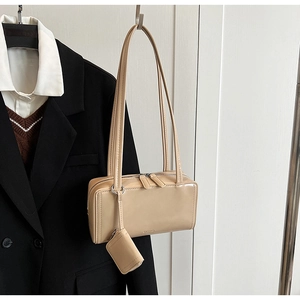 Dettaglio borsa sottobraccio in pelle lucida beige con pochette su un abito nero