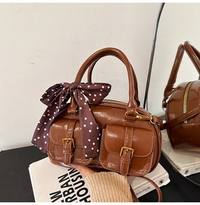 Detail of dark brown glossy Boston bag featuring front pockets and decorative polka dot bow