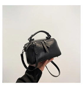 Detail of glossy black leather crossbody bag featuring top handle and metallic zippers
