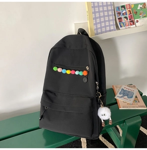 Detail of black casual backpack featuring colorful pom-poms and a cute monster pendant