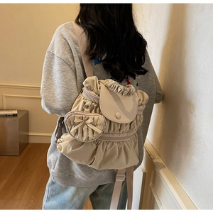 Detailed view of beige pleated backpack with heart-shaped pouch and bow decoration