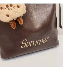 Detail of dark brown faux leather tote with Summer embroidery and plush biscuit charm