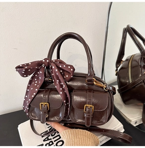 Detail of dark brown glossy bowling bag with gold buckles and polka dot silk scarf