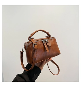 Close-up of brown bucket bag showing wax-finished leather texture and dual zippers