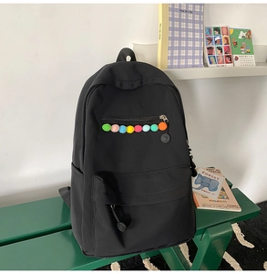 Detail of black backpack with colorful pom-poms on a green bench in a lifestyle setting