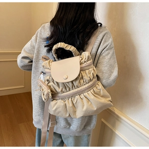 Detail of beige pleated nylon backpack with double zippers and small round side pouch