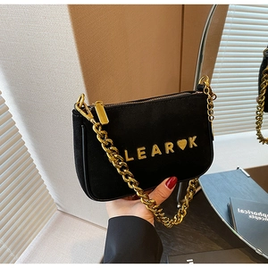 Close-up of black suede underarm bag featuring a chunky gold chain and metal logo