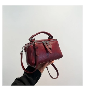 Detail view of burgundy box bag with glossy textured leather and dual metal zippers
