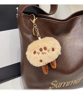 Close-up of a beige plush ball pendant with gold clasp on a brown leather tote bag
