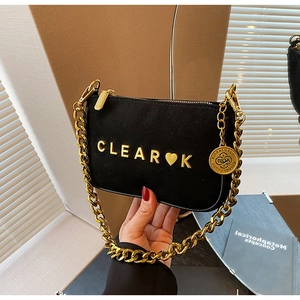 Detail of black suede shoulder bag with gold metal chain and heart letter plaque