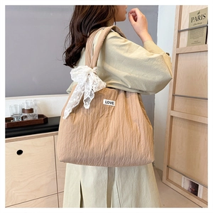 Detail of light khaki pleated tote bag featuring white lace bow and LOVE patch