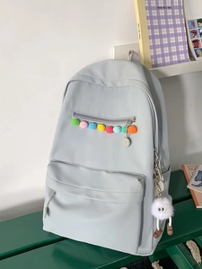 Light blue canvas backpack with colorful pom-poms and cute plush pendant on wooden bench