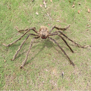 Detailed view of giant hairy spider prop with red eyes and flexible legs on grass