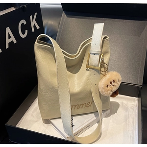 Detail view of cream tote bag with adjustable shoulder strap and plush bear charm in gift box