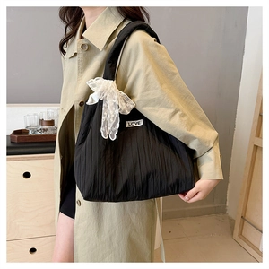 Detail of black pleated tote bag featuring a large white lace bow and LOVE textile label